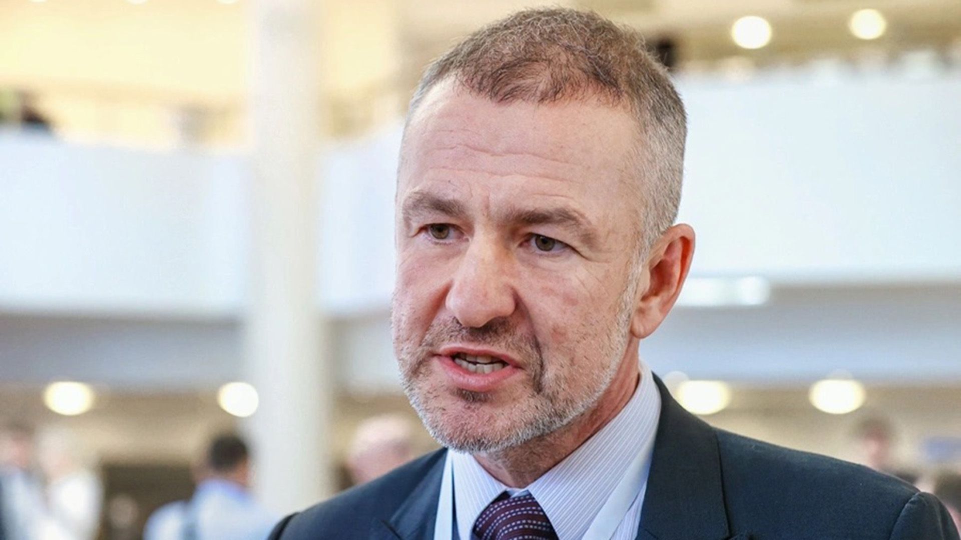 Андрей Мельниченко в сером пиджаке смотрит в сторону и что-то говорит